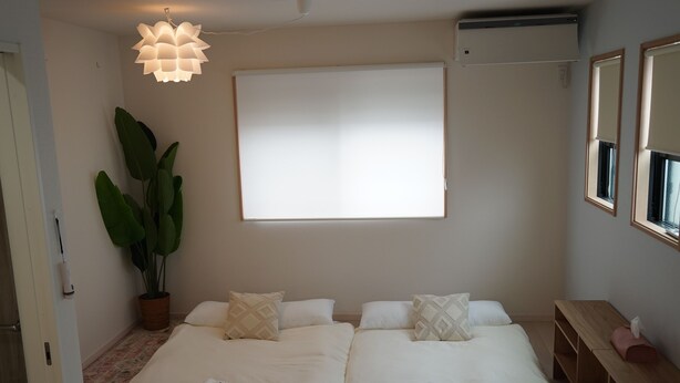 Quarto de hotel com uma cama, uma janela grande, uma planta em vaso e um lustre.