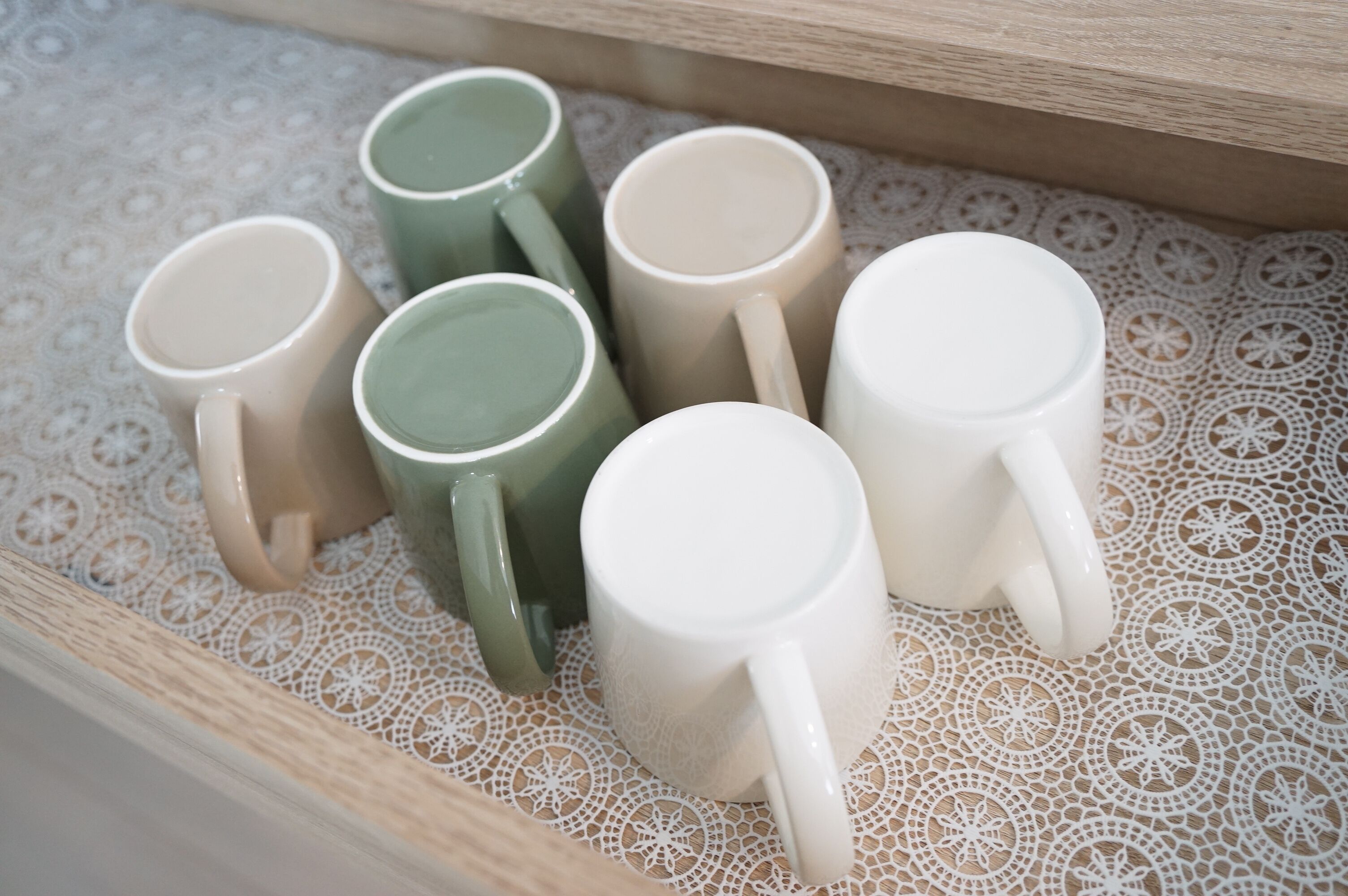 Un ensemble de cinq tasses en céramique disposées sur une nappe en dentelle.