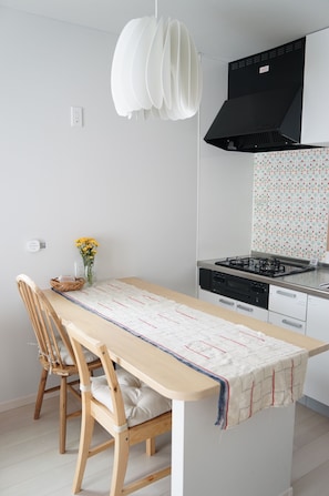 A modern kitchen with a gas stove, a black range hood, and a white pendant light.