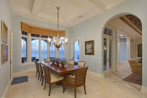 A dining room with a large table, chairs, a chandelier, and large windows with a view.