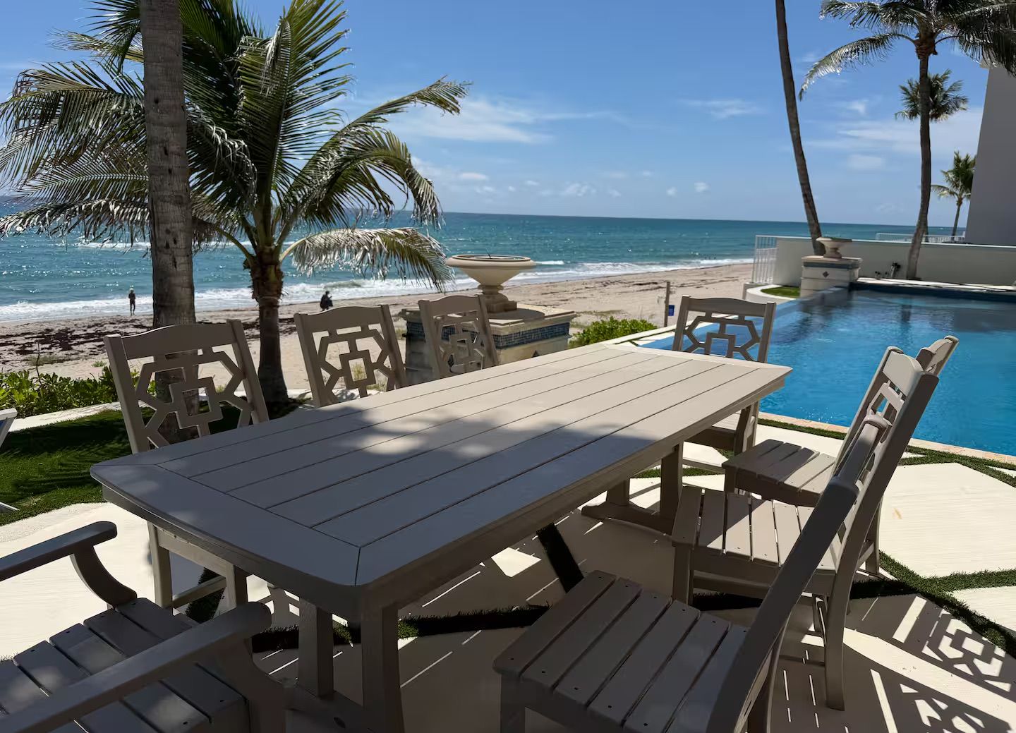 A poolside area with a table and chairs, overlooking a beach and ocean.