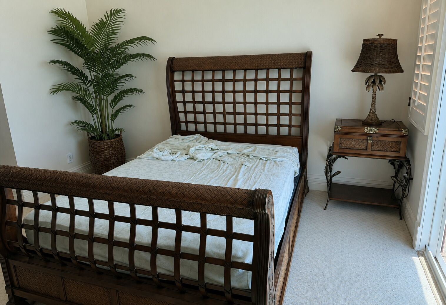 Een slaapkamer met een houten bed, een nachtkastje, een lamp en een potplant.