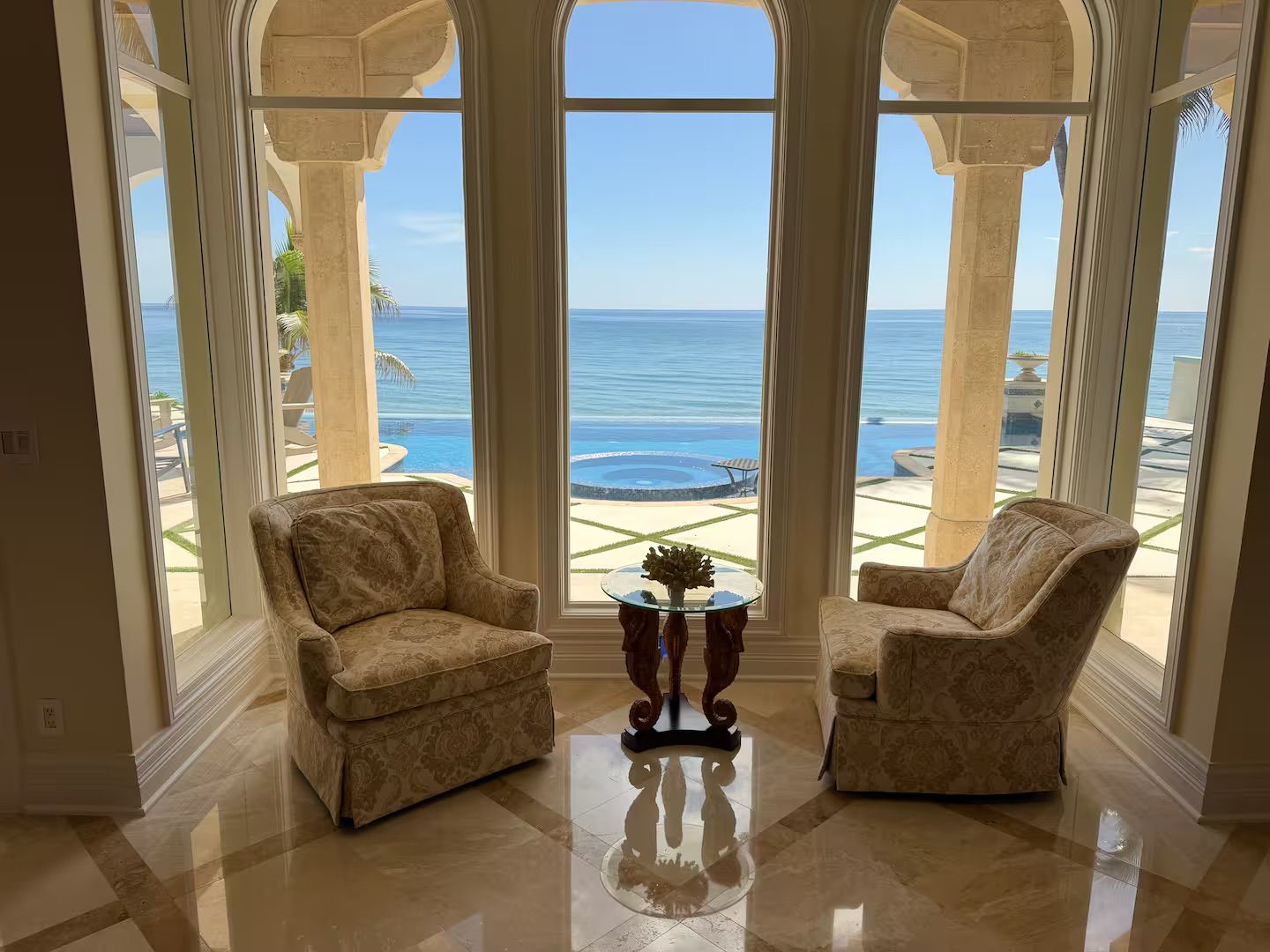 Habitación con dos sillones frente a un ventanal con vista a una playa y piscina.