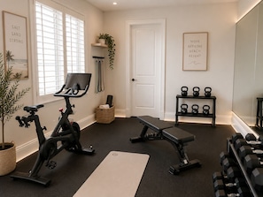 A home gym with exercise equipment, a bench, a yoga mat, and motivational wall art.