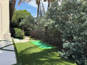 A well-maintained garden with a paved patio, a green artificial turf area, and a metal fence.