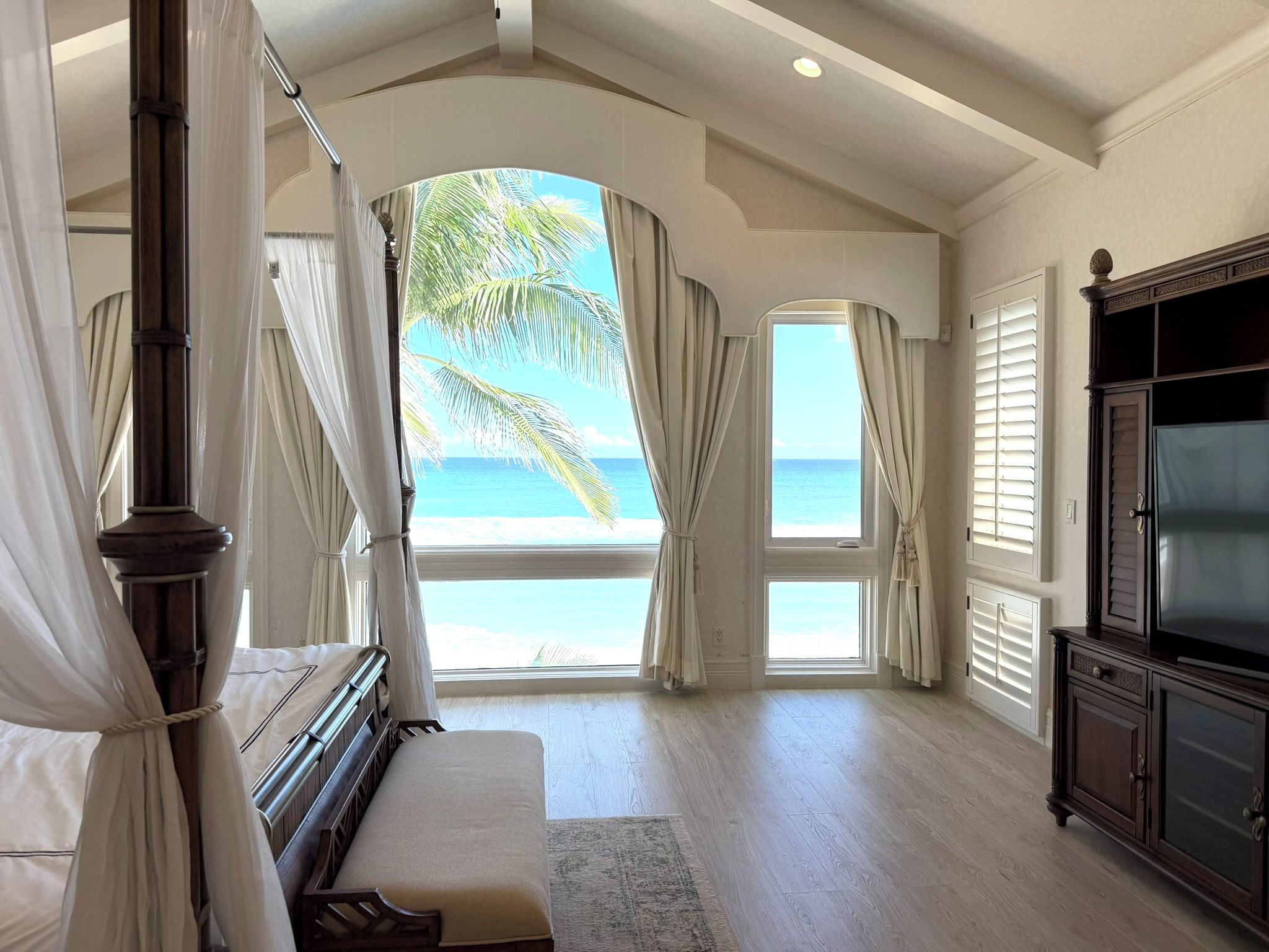 A bedroom with a large bed, a TV, and a view of the beach.
