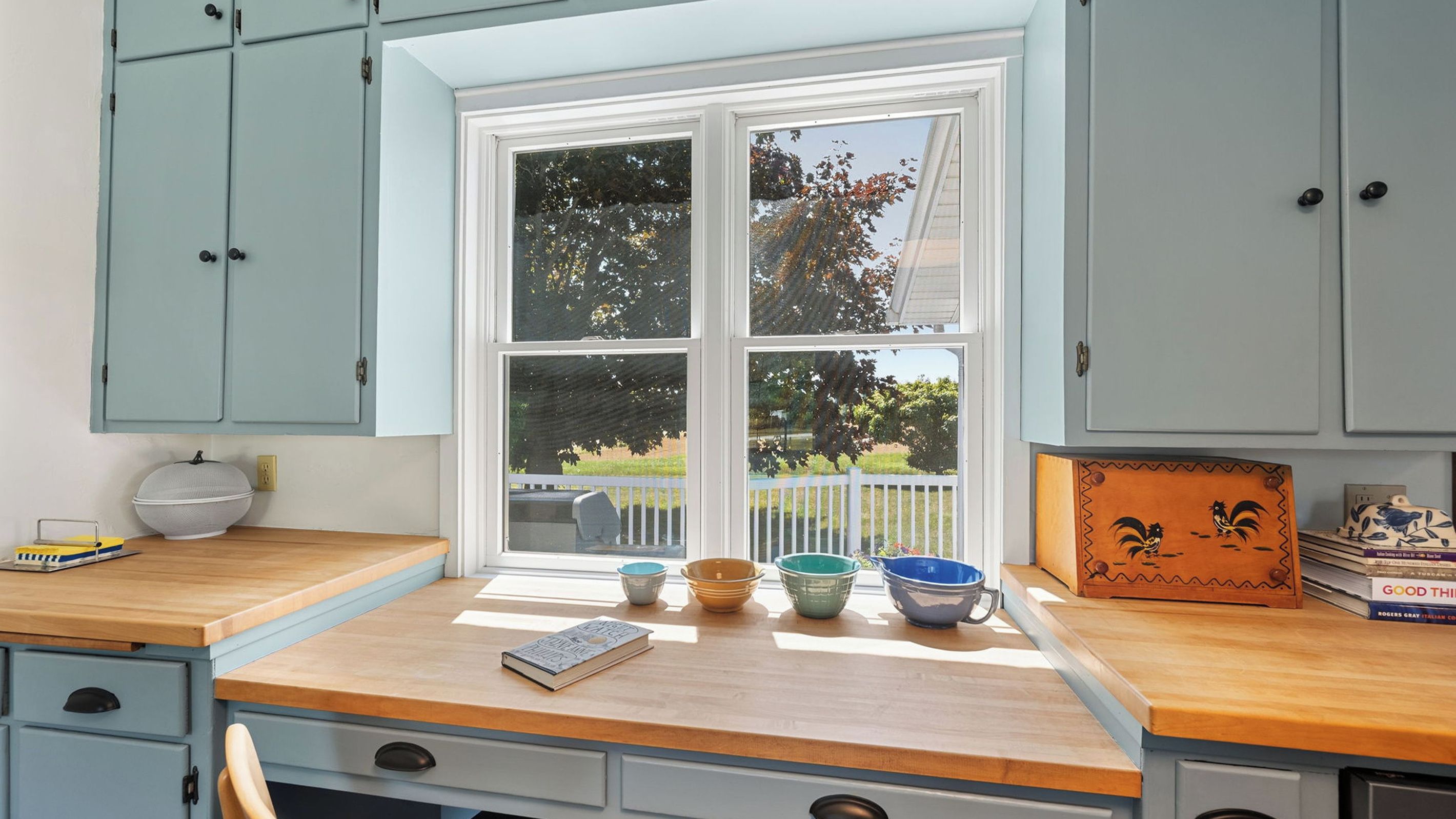 A kitchen with a bay window, wooden countertop, and various kitchenware.