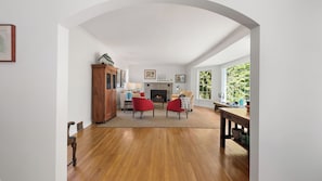 A living room with a fireplace, wooden flooring, and a view of greenery outside.