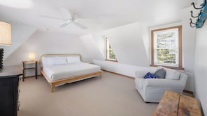 A bedroom with a bed, a sofa, a desk, a lamp, a ceiling fan, and a window with blinds.