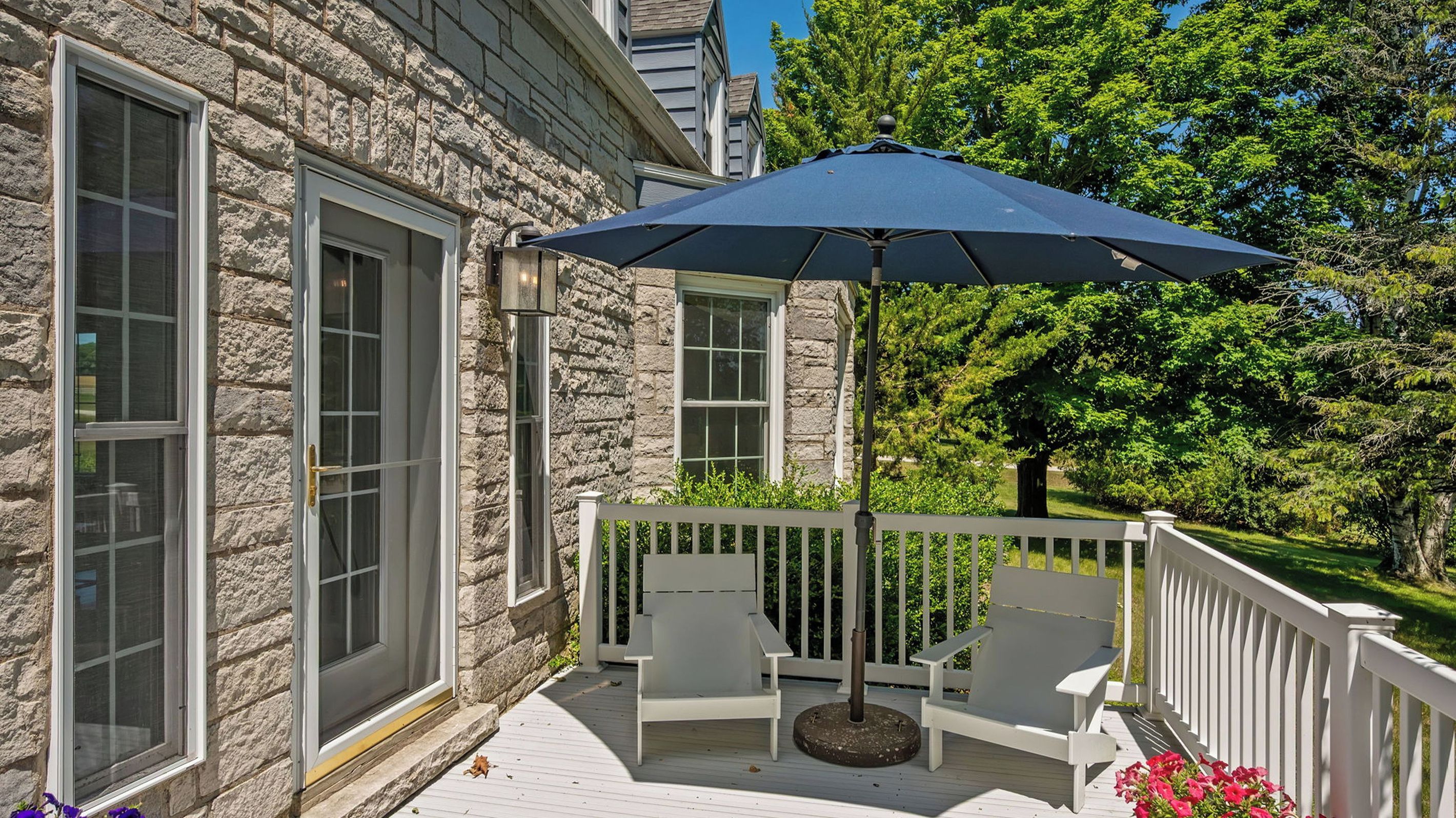 A stone building with a wooden deck, two chairs, and a large umbrella.