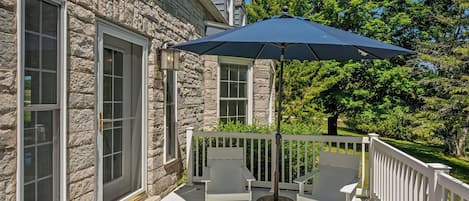 Een gebouw van steen met een houten terras, twee stoelen en een grote parasol.
