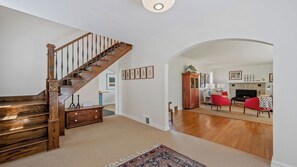 Un salón amplio con una escalera de madera, una chimenea y un sillón rojo.