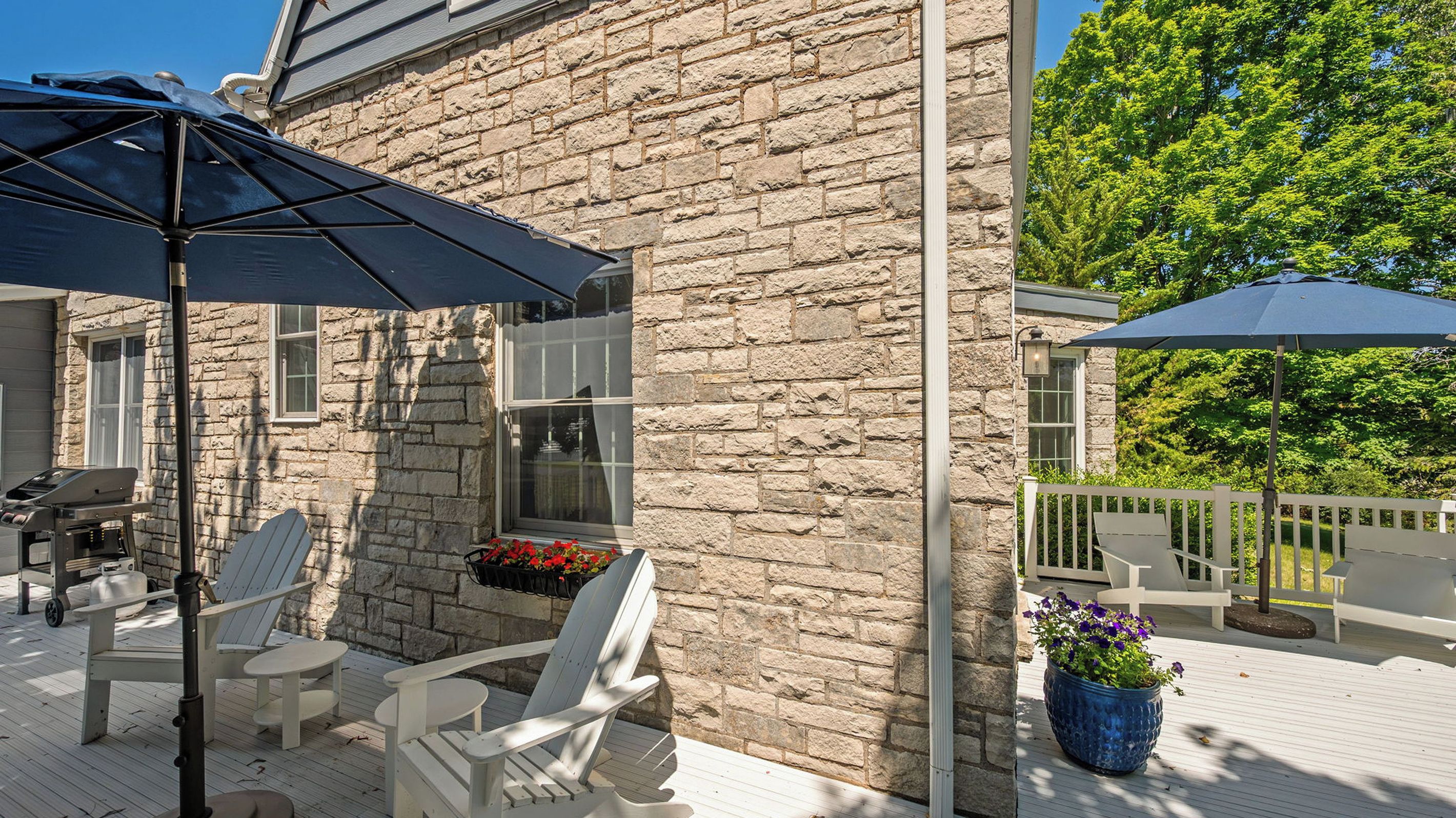 A stone building with a deck, outdoor seating, and a barbecue grill.