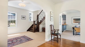 A spacious room with a wooden staircase, a dining area with a table and chairs, and a view of a blue kitchen.