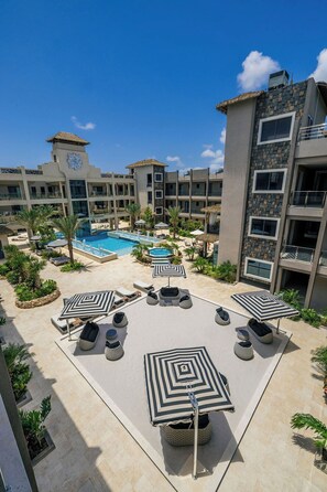 A resort with a swimming pool, lounge chairs, and a thatched-roof building. - Brand New Walishali 1BR Condo  Close 2 EagleBeach (Noord)
