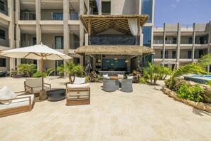 A resort's outdoor seating area with lounge chairs, a thatched-roof structure, and a poolside view. - Brand New Walishali 1BR Condo  Close 2 EagleBeach (Noord)