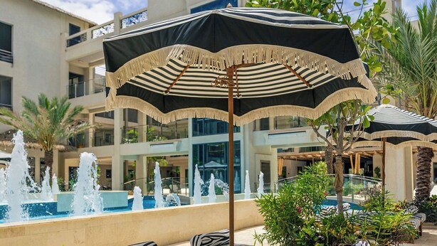 Un área junto a la piscina con sillones y sombrillas, una fuente y un edificio con una fachada llamativa.