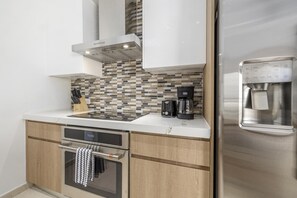 Eine kompakte Küche mit Einbauofen, Kaffeemaschine und Wasserspender am Kühlschrank.