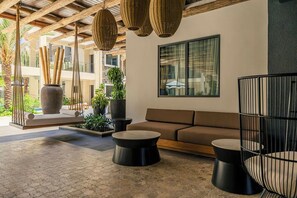 A modern lounge area with a sofa, two round tables, hanging wicker lamps, and a large window. - Brand New Walishali 1BR Condo  Close 2 EagleBeach (Noord)