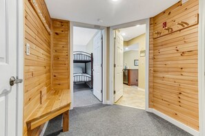 A hallway with wooden paneling, a bench, and a bunk bed in the background.