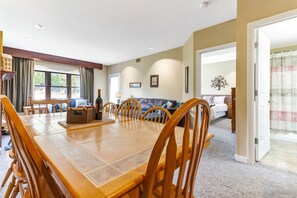A dining area with a wooden table and chairs, a bottle of wine, and a basket.