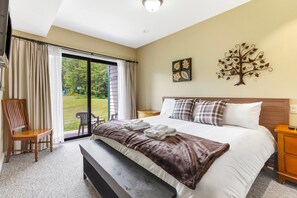 A hotel room with a bed, a bench, a chair, a desk, and a large window with curtains.