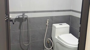 A small bathroom with a toilet, a shower, and a hand dryer. - HB Apartment Lang (Hanoi)
