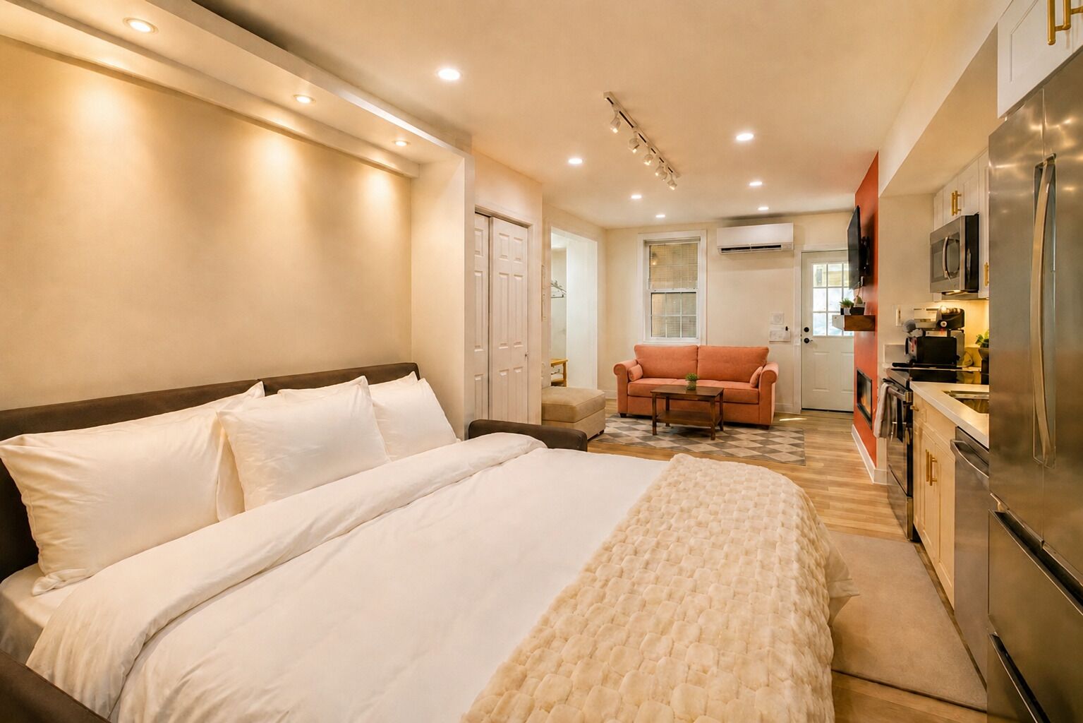 A hotel room with a large bed, a sofa, a kitchenette, and a bathroom.