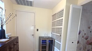 A room with a wooden floor, a white door, a cabinet, a small refrigerator, and a decorative wall panel. - Memories Beach Villa! Near Gulf Beaches + BBQ (Largo)