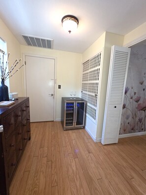 A room with a wooden floor, a white door, a cabinet, a small refrigerator, and a decorative wall panel. - Memories Beach Villa! Near Gulf Beaches + BBQ (Largo)