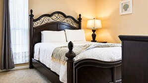 A bedroom with a dark wooden bed frame, white bedding, a bedside lamp, and a framed picture on the wall. - Memories Beach Villa! Near Gulf Beaches + BBQ (Largo)