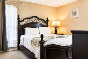 A bedroom with a dark wooden bed frame, white bedding, a bedside lamp, and a framed picture on the wall. - Memories Beach Villa! Near Gulf Beaches + BBQ (Largo)
