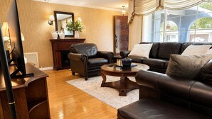 A living room with a leather sofa, a coffee table, a fireplace, and a large window with curtains. - Memories Beach Villa! Near Gulf Beaches + BBQ (Largo)