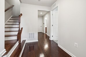 A clean, modern hallway with a wooden staircase, white walls, and a vent on the floor. - Your Oasis Away From Home, 4-bedroom townhome in Greenbelt (Greenbelt)