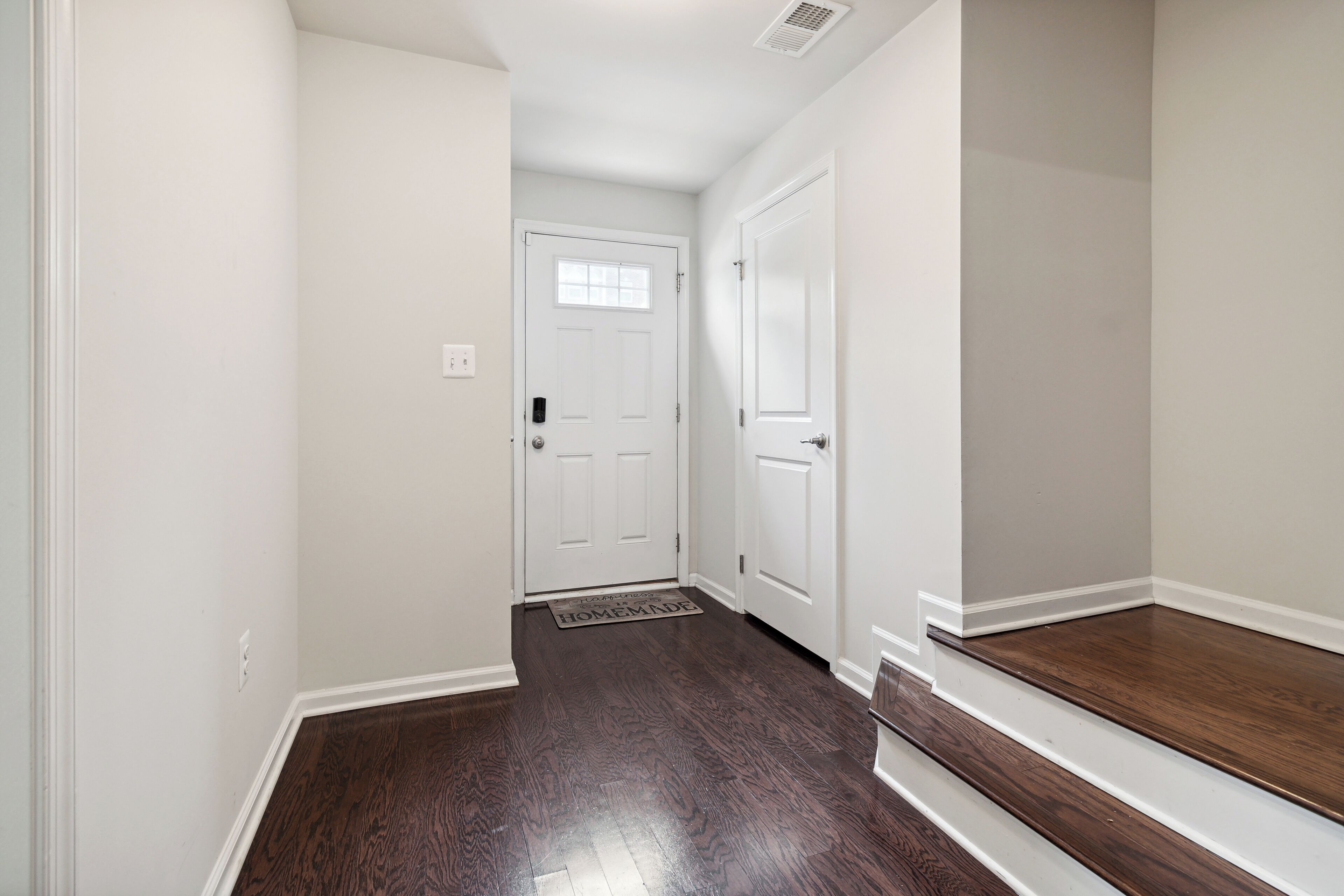 A hallway with two white doors, a doormat, and a wooden floor.