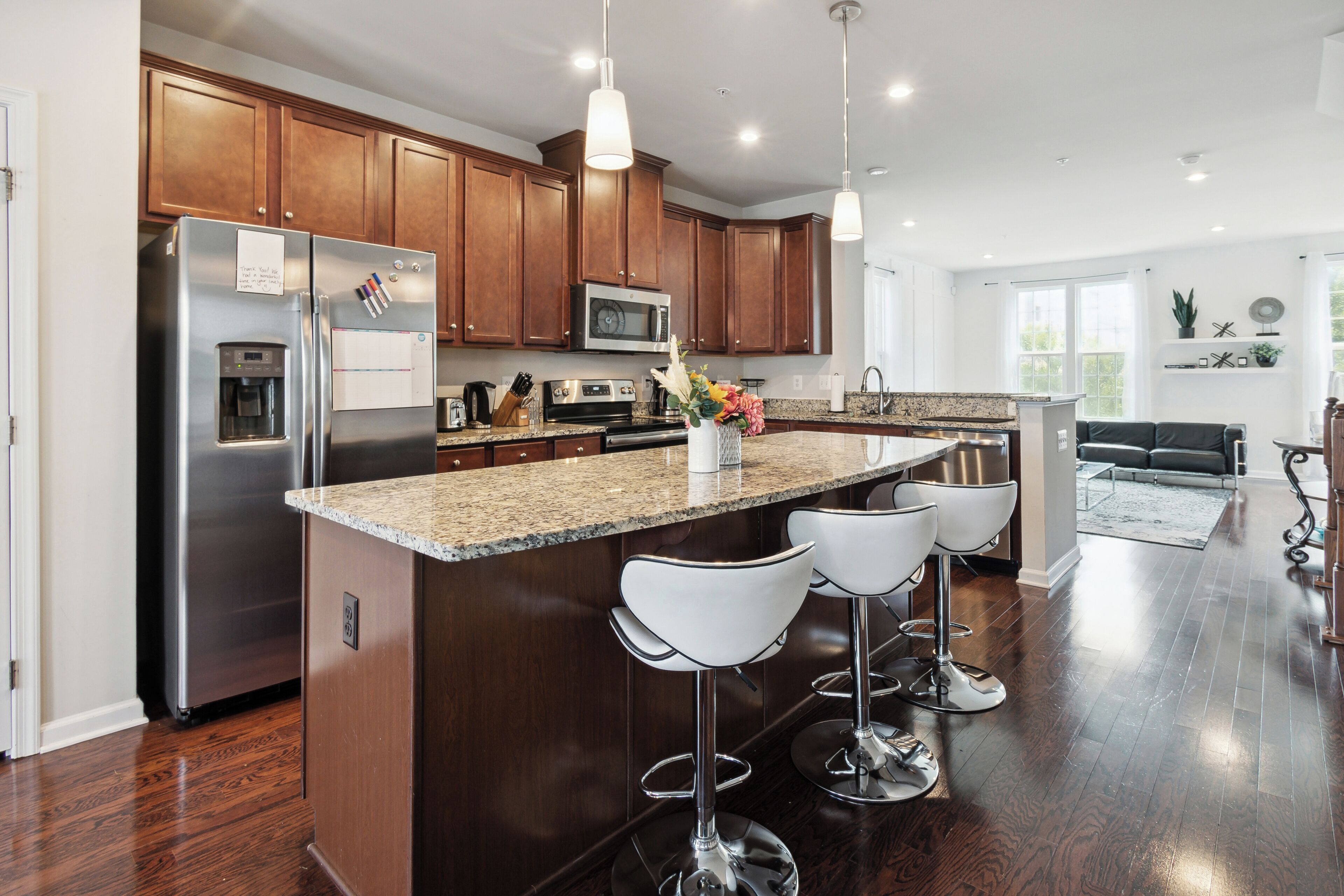 Una cocina moderna con una isla central, electrodomésticos de acero inoxidable, armarios de madera e iluminación colgante.