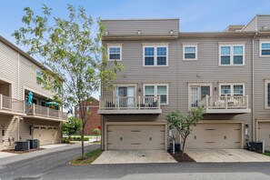 A multi-story residential building with a garage, balconies, and a tree in the driveway. - Your Oasis Away From Home, 4-bedroom townhome in Greenbelt (Greenbelt)