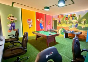 Ein Raum mit Pooltisch, zwei Spieltischen und farbenfroher Wandgestaltung, darunter Figuren aus Mario's Welt.