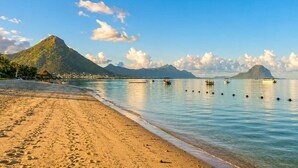 A beach with clear water, a mountain in the background, and boats. - 3BR Sunset Sea View, Steps to Flic en Flac Beach (Flic en Flac)