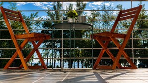A patio with two wooden chairs and a round table, a metal railing, and a view of the ocean. - 3BR Sunset Sea View, Steps to Flic en Flac Beach (Flic en Flac)