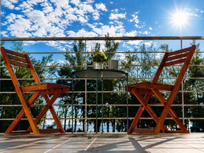 A patio with two wooden chairs and a round table, a metal railing, and a view of the ocean. - 3BR Sunset Sea View, Steps to Flic en Flac Beach (Flic en Flac)