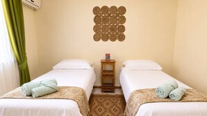 A hotel room with two beds, a small wooden nightstand, a decorative wall hanging, and a patterned floor. - 3BR Sunset Sea View, Steps to Flic en Flac Beach (Flic en Flac)