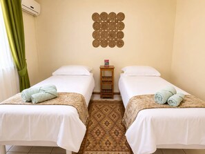 A hotel room with two beds, a small wooden nightstand, a decorative wall hanging, and a patterned floor. - 3BR Sunset Sea View, Steps to Flic en Flac Beach (Flic en Flac)