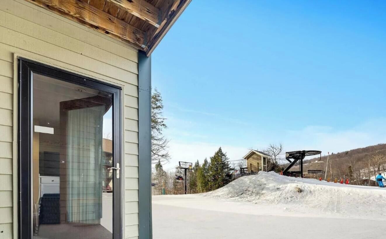 Un bâtiment avec une entrée dotée d’une porte en verre, un télésiège en arrière-plan et une pente enneigée.