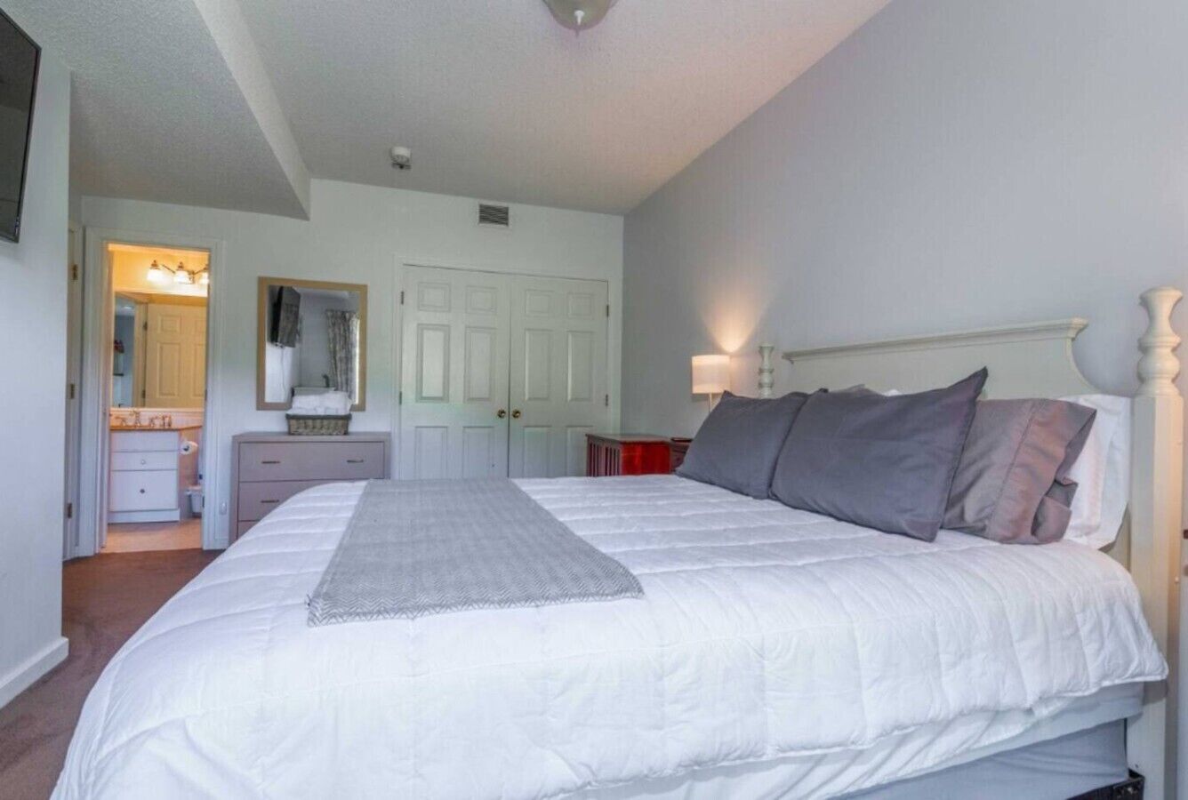 A bedroom with a large bed, a dresser, a mirror, and a door leading to a bathroom.