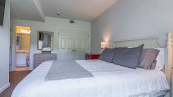 A bedroom with a large bed, a dresser, a mirror, and a door leading to a bathroom.