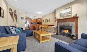A living room with a fireplace, a dining area, and a kitchen in the background.