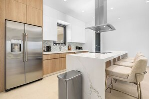 A modern kitchen with a stainless steel refrigerator, a coffee machine, and a marble countertop. - Brand New Top Floor 2BR2BA Condo near Eagle Beach (Oranjestad)