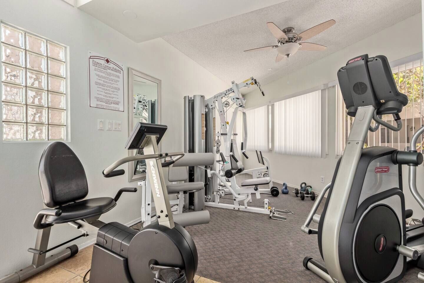A gym with cardio machines, weightlifting equipment, and a ceiling fan.