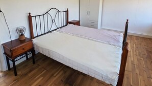 A bedroom with a wooden floor, a bed with a metal headboard, a nightstand with a lamp, and a wardrobe. - 2 Person Holiday Home in Vra (Vra)